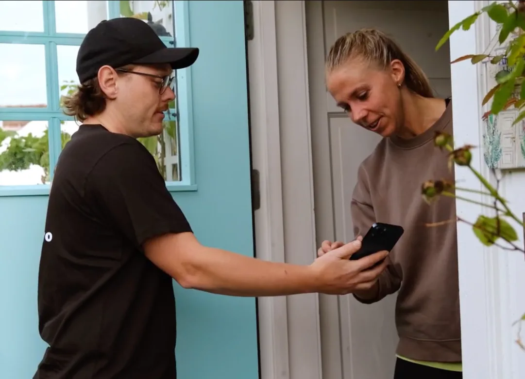 Håndverker viser tilbudet til kunden i døra, som signerer på mobilen